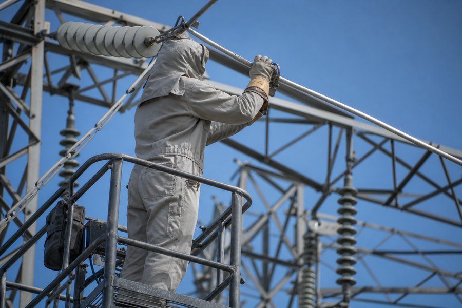 Linesworker in arc-rated workwear on a transmission structure
